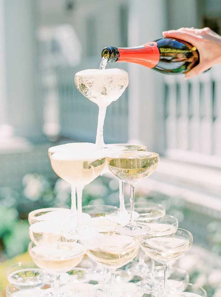 Champagne is poured into a cascading tower of glasses, outdoors.