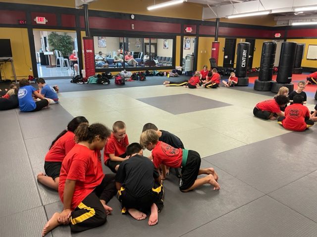 A group of kids are kneeling on the floor in a gym