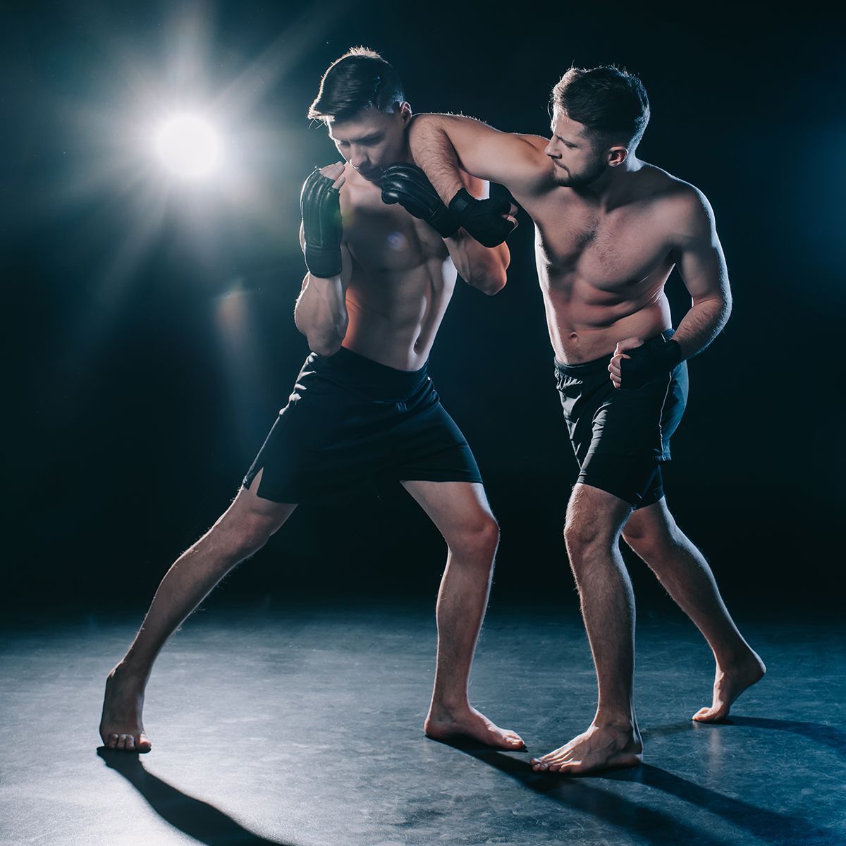 two men are fighting in a dark room with a light behind them