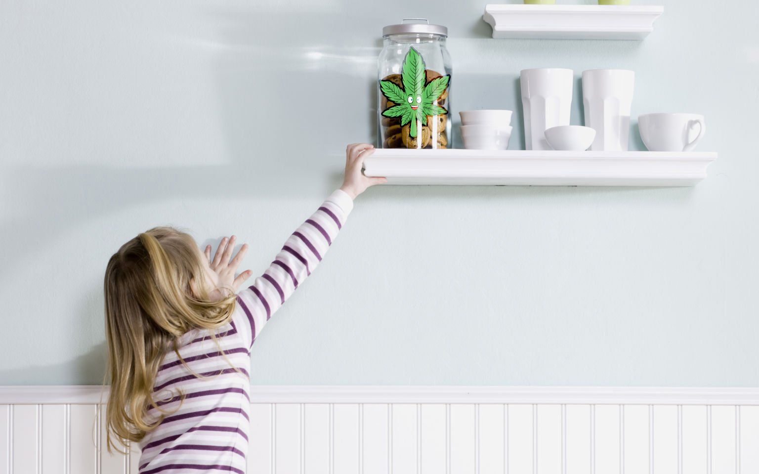 A little girl is reaching for a shelf on a wall.