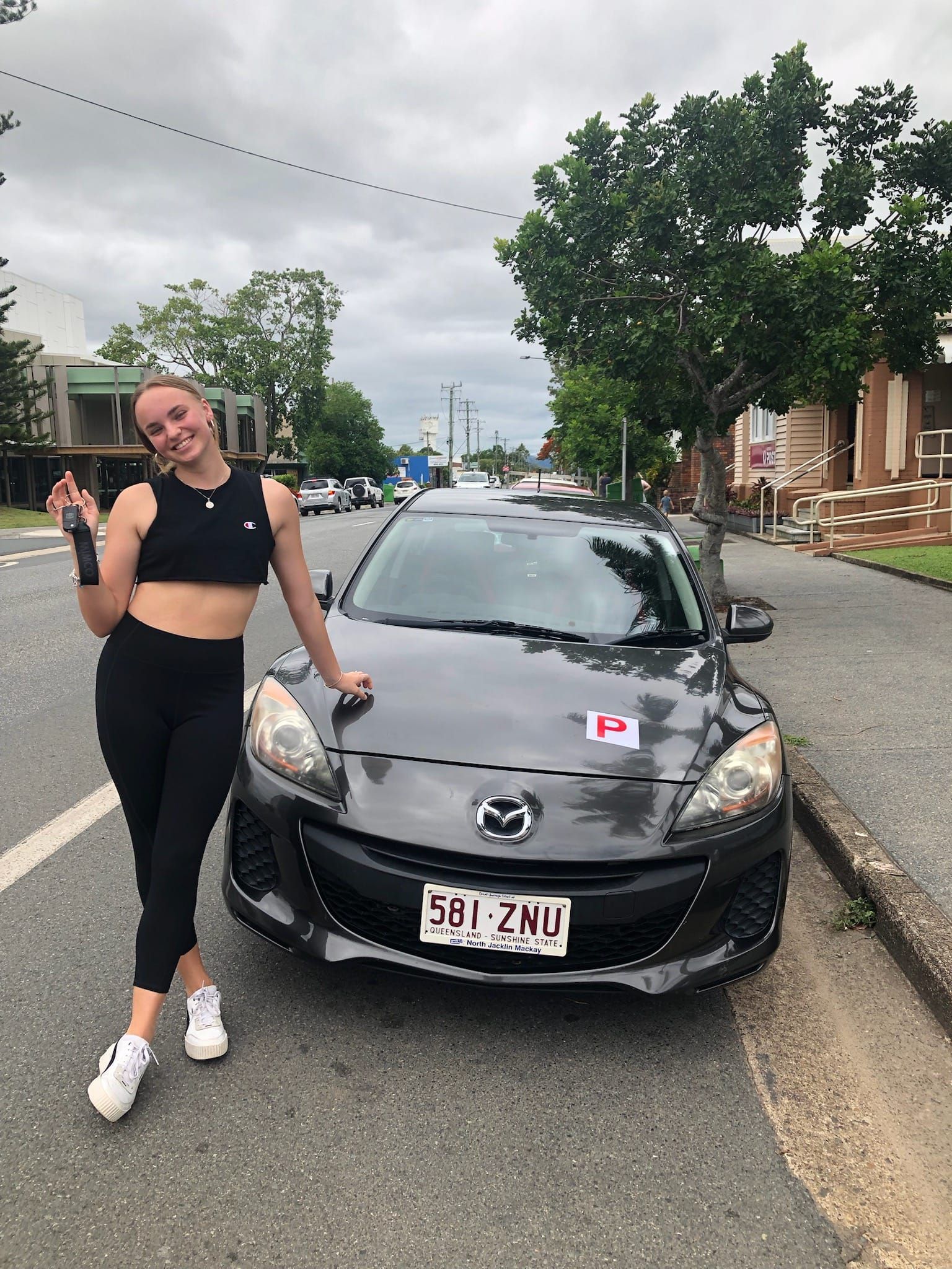 Woman in black athletic wear leans on a gray Mazda 3 on a street — Top Start Driving School (Whitsunday) In Airlie Beach, QLD