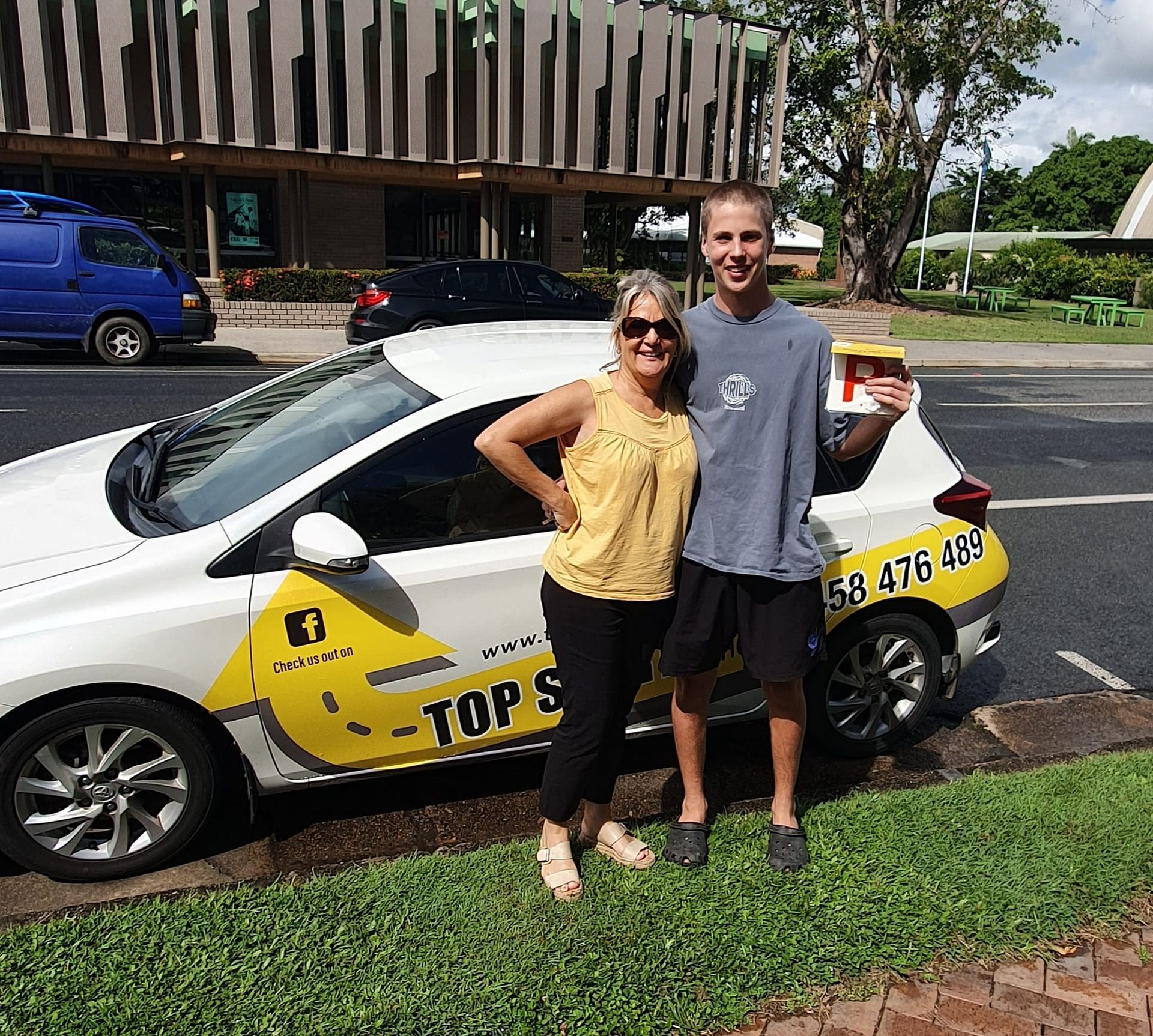 Woman and teen pose next to a car with “Top Slice” logo; teen holds pizza box.