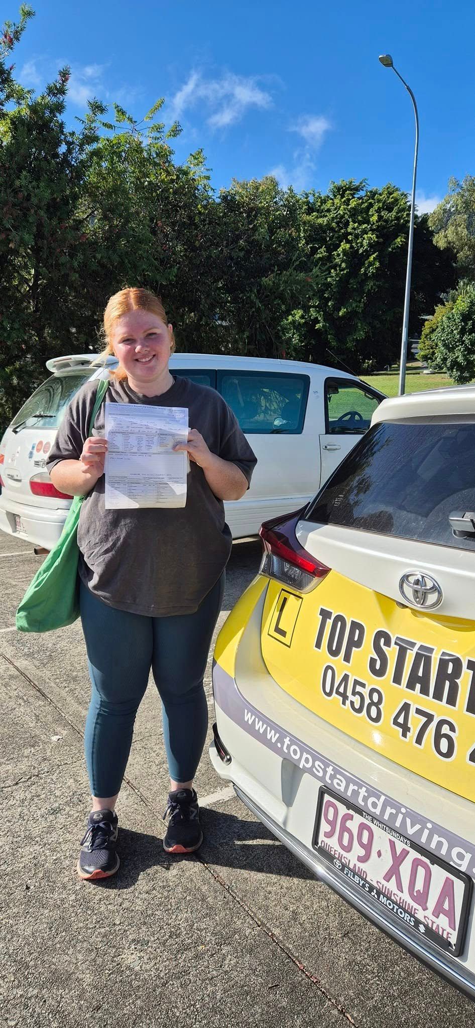 Woman Holding Paperwork Smiles in Front of a White Car — Top Start Driving School (Whitsunday) In Airlie Beach, QLD
