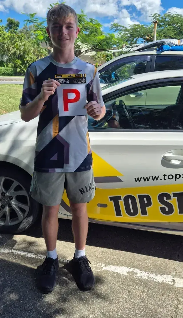 Teen holding a P-plate next to a white car with 