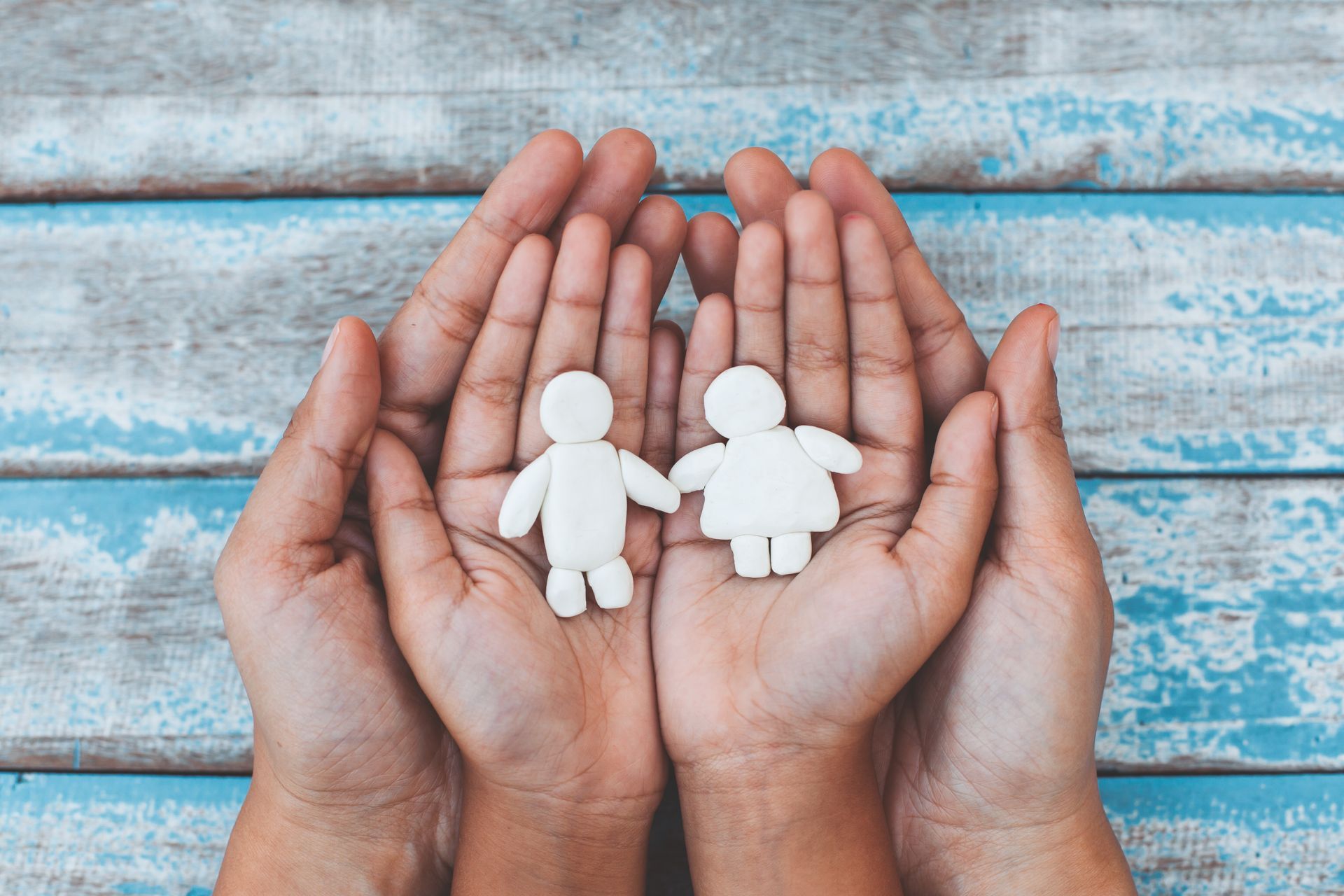A person is holding two paper dolls in their hands.