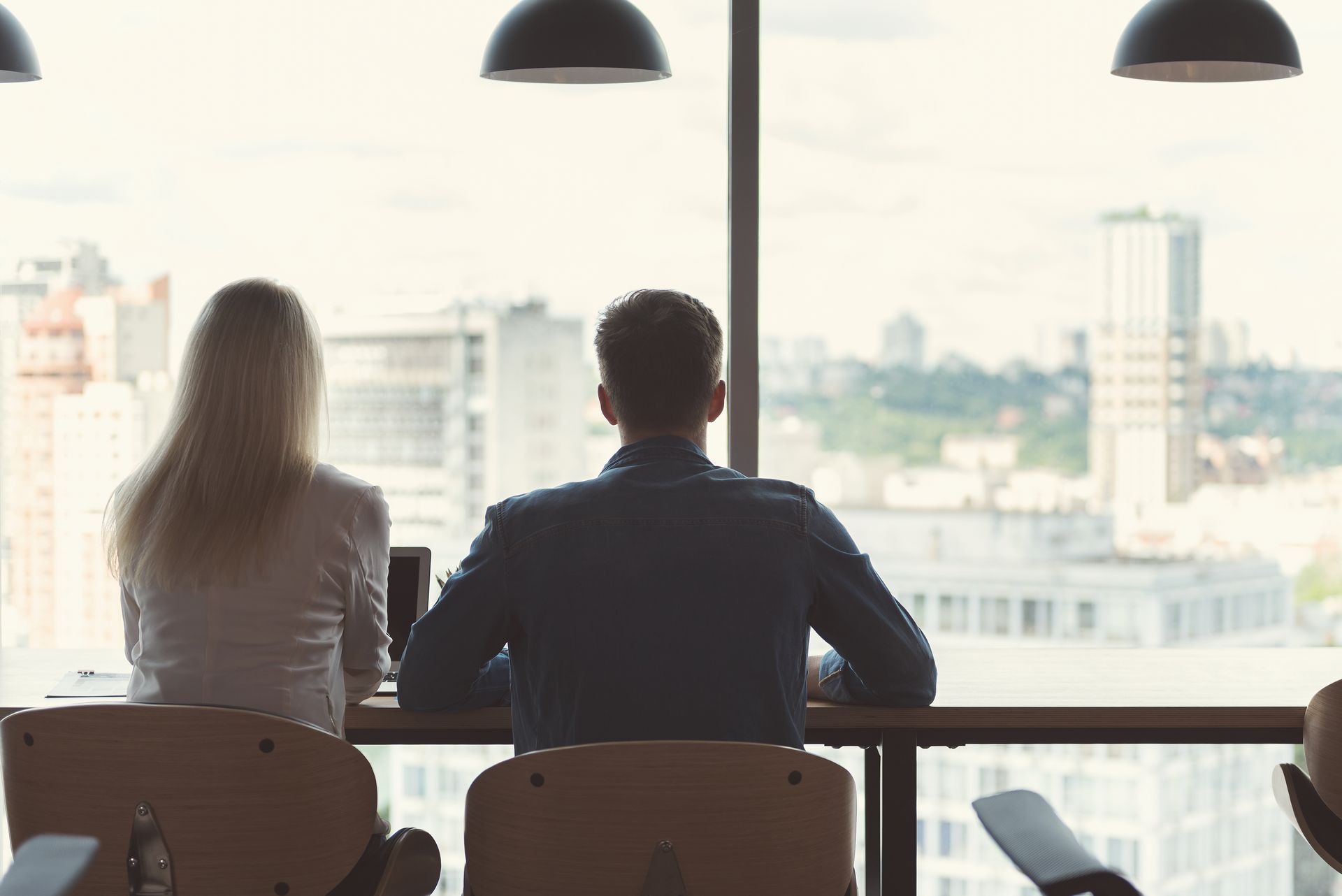 A man and a woman are sitting at a table looking out a window.