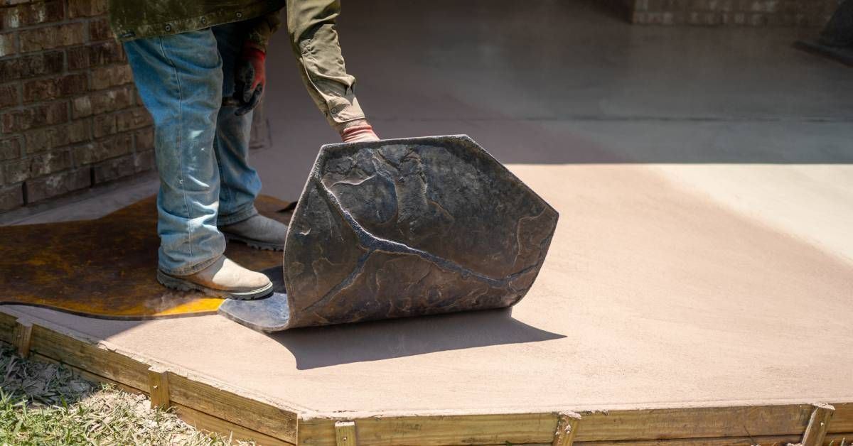 A concrete contractor laying a decorative concrete mold onto a freshly poured concrete slab in front