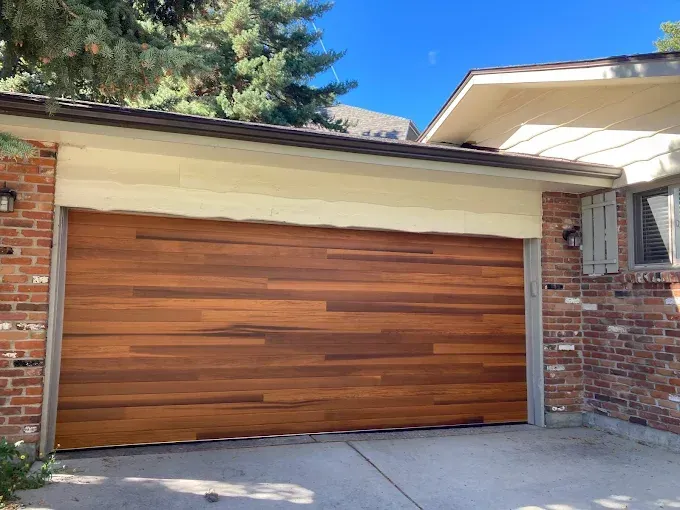Wooden garage door on a brick house with a concrete driveway and blue sky above