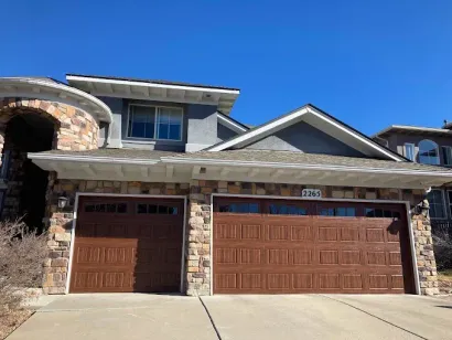 Two-story stone house with a brown double garage door under a bright blue sky