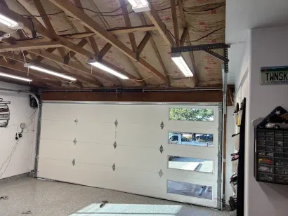 Interior of a garage with white overhead door, exposed wooden rafters, and fluorescent lights