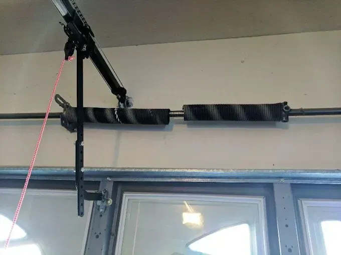 Black garage door opener mounted above a window, with a red pull cord hanging down.