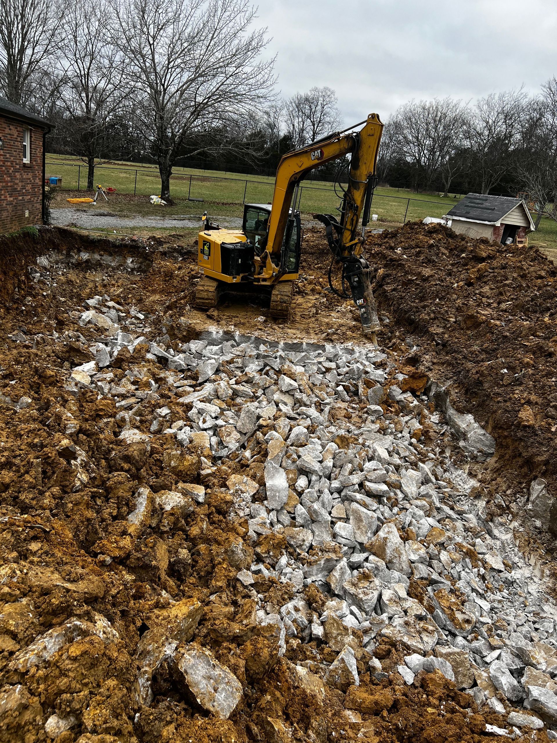 A yellow excavator is digging a hole in a pile of rocks.