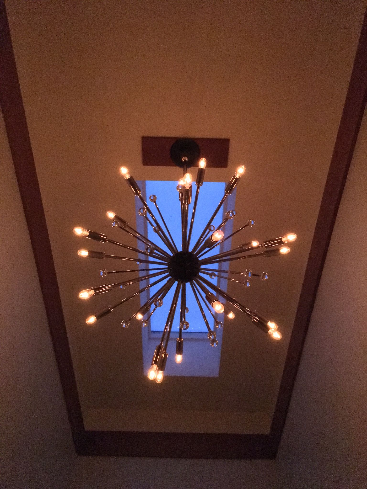 A chandelier hanging from the ceiling with a skylight in the background
