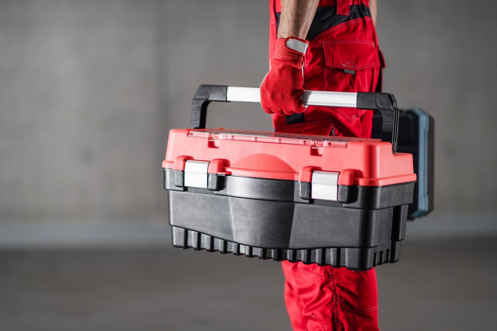A man in red overalls is holding a red and black toolbox.