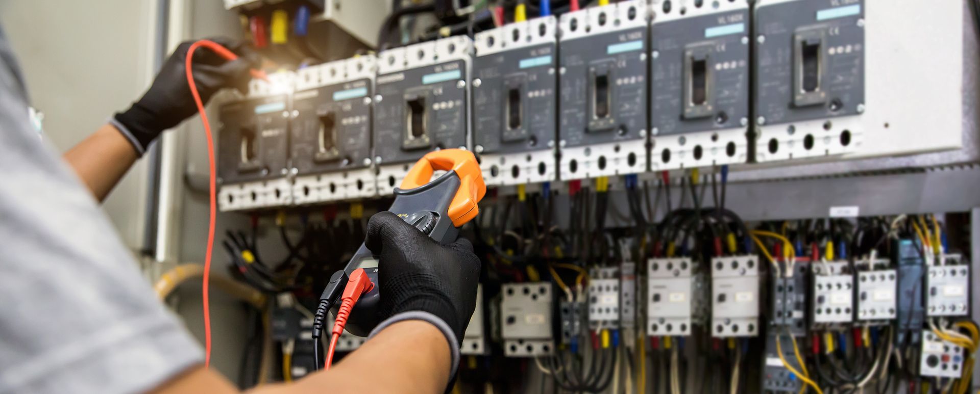 A man is working on an electrical panel with a multimeter.