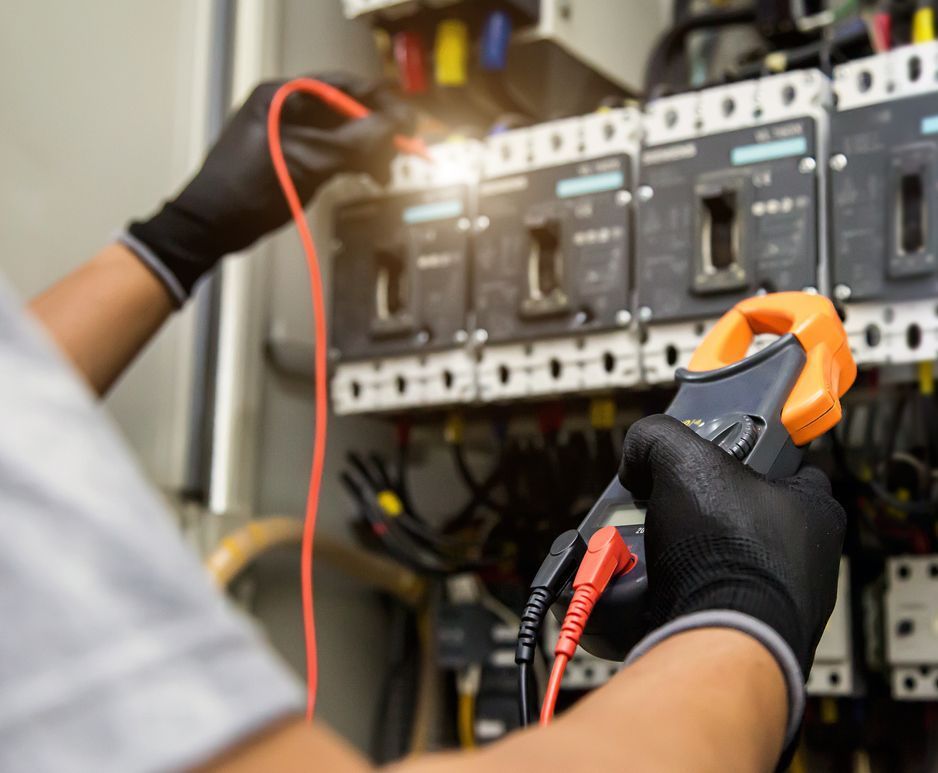 An electrician is working on an electrical box with a clamp meter.