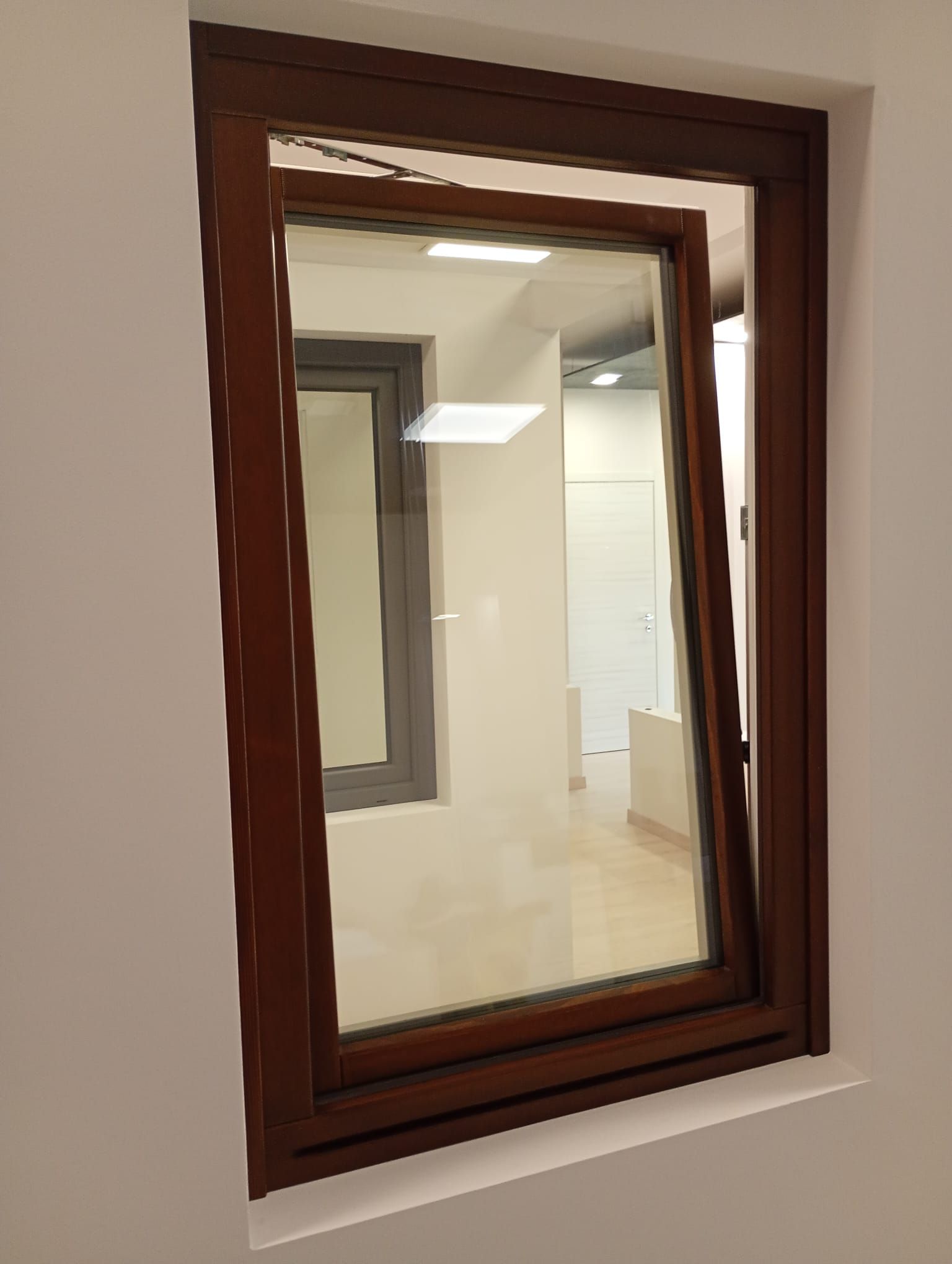 Una finestra con cornice marrone incastonata in una parete bianca, posizionata leggermente aperta per consentire la ventilazione.