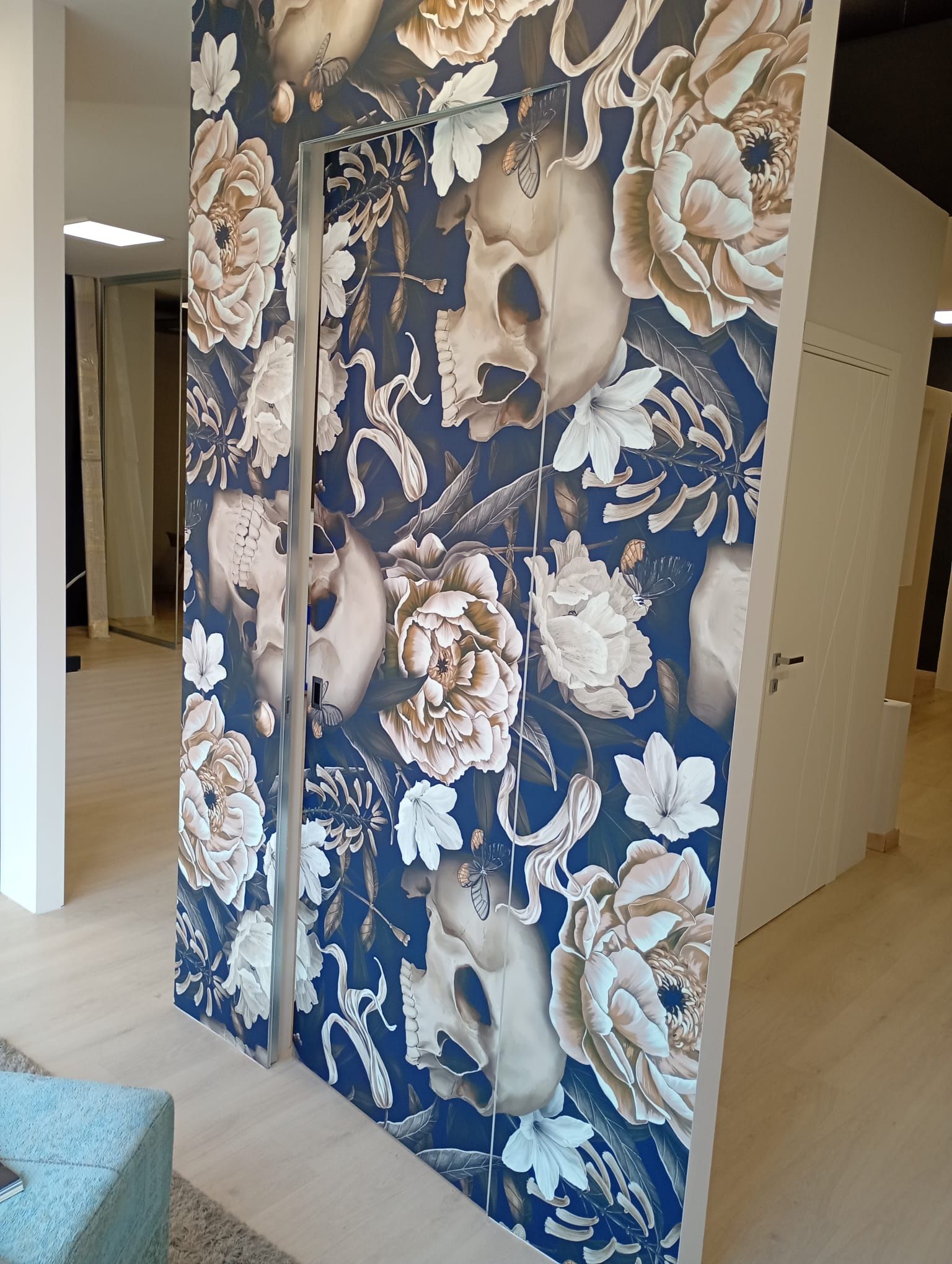 Una porta rivestita di carta da parati con uno sfondo blu scuro e un motivo ripetuto di fiori bianchi e teschi umani.