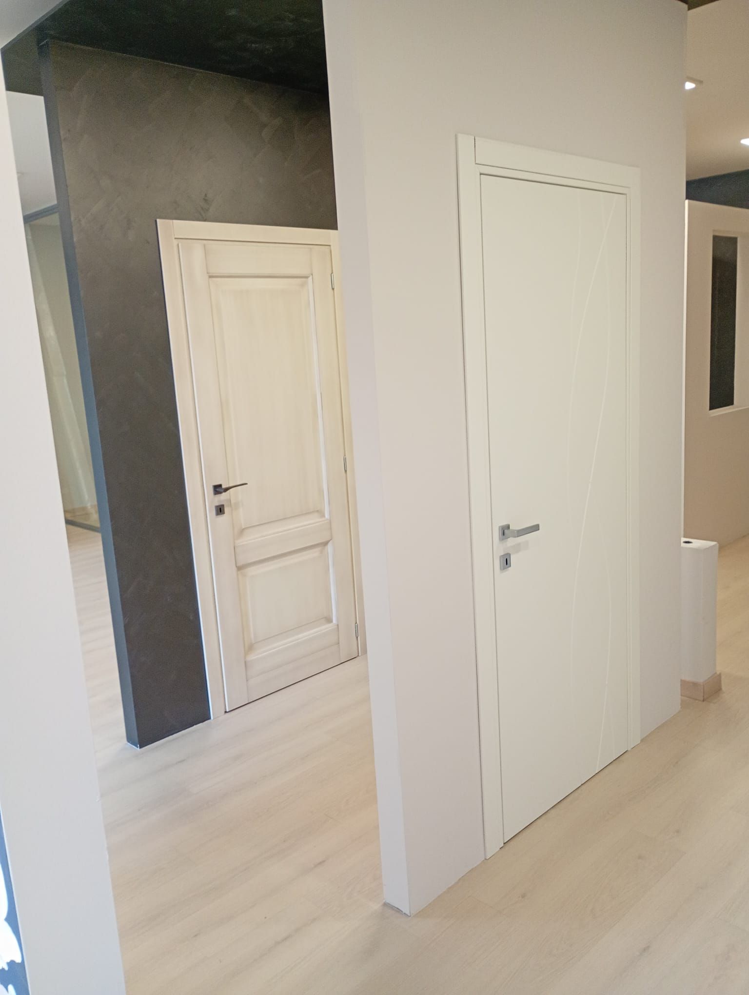 Vista di un interno moderno con una semplice porta bianca in primo piano e una classica porta bianca a pannelli sullo sfondo.
