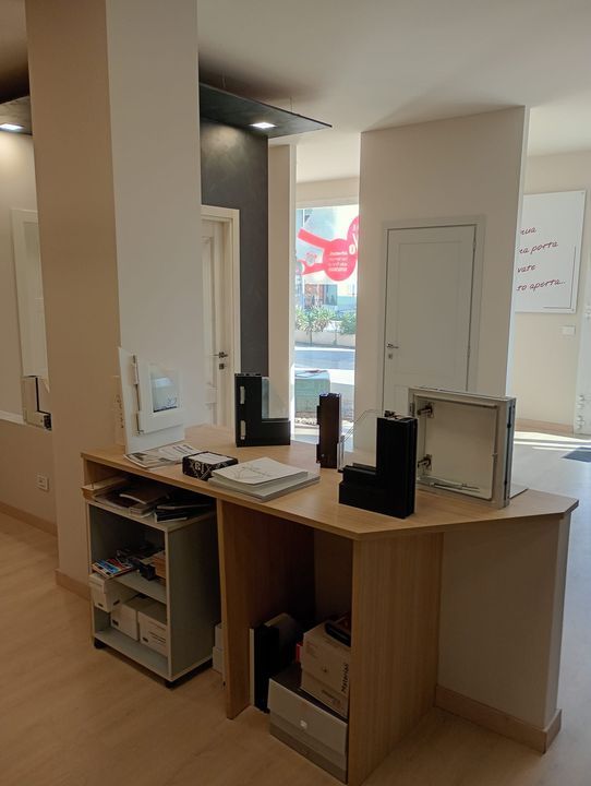 Un bancone reception in legno in un interno moderno, con diversi campioni di infissi e articoli per ufficio sul bancone.