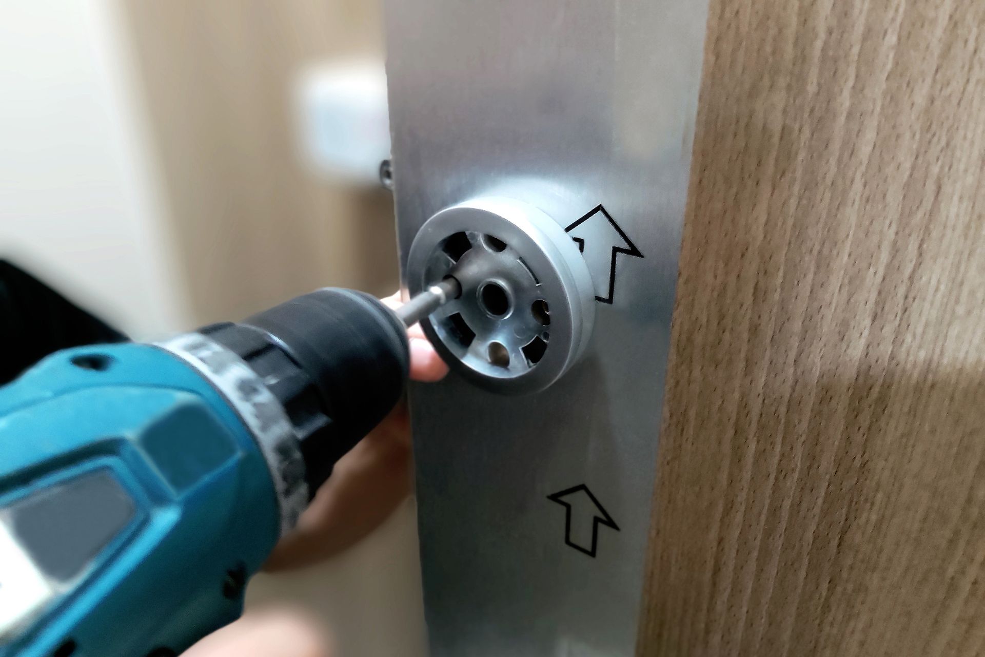 Si sta utilizzando un trapano per fissare una staffa di montaggio circolare a un pannello metallico contrassegnato da frecce rivolte verso l'alto.