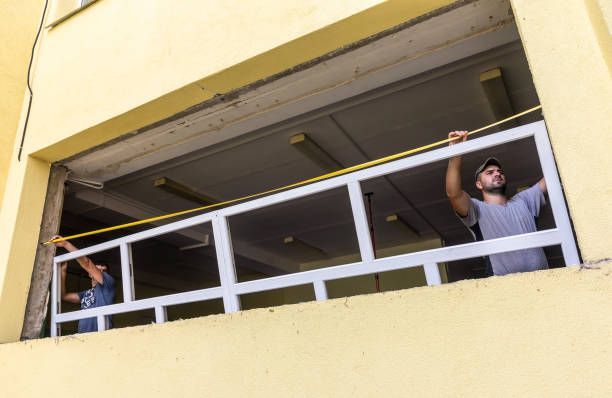 Due operai utilizzano un metro a nastro giallo per misurare la larghezza di un'apertura di una finestra in un edificio giallo.