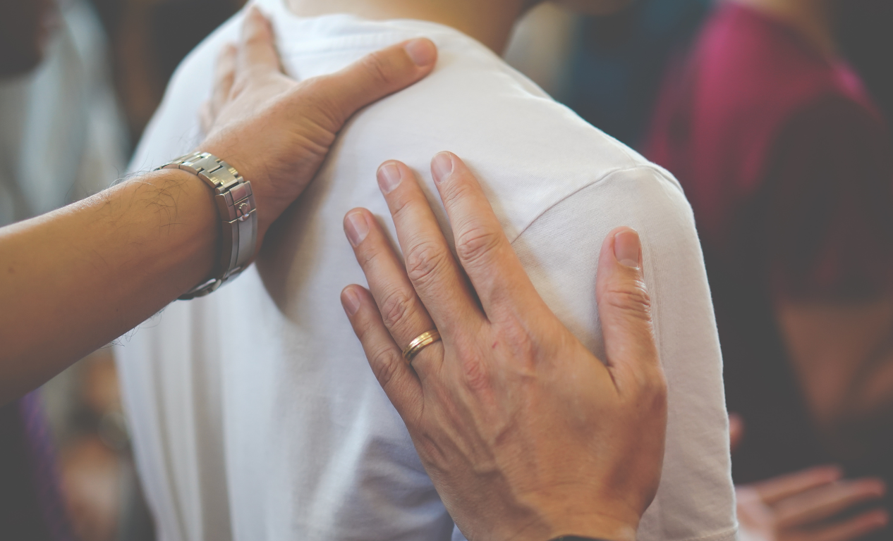 Hand on the shoulder of a person in a white shirt, showing support or comfort.