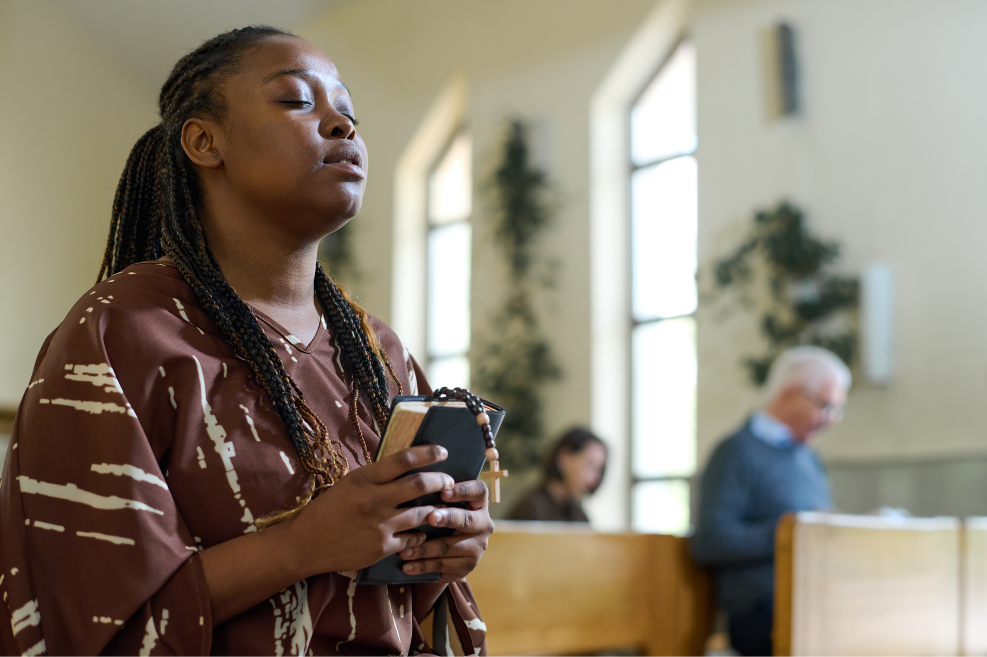 Woman holding a book and beads, eyes closed in prayer inside a church.