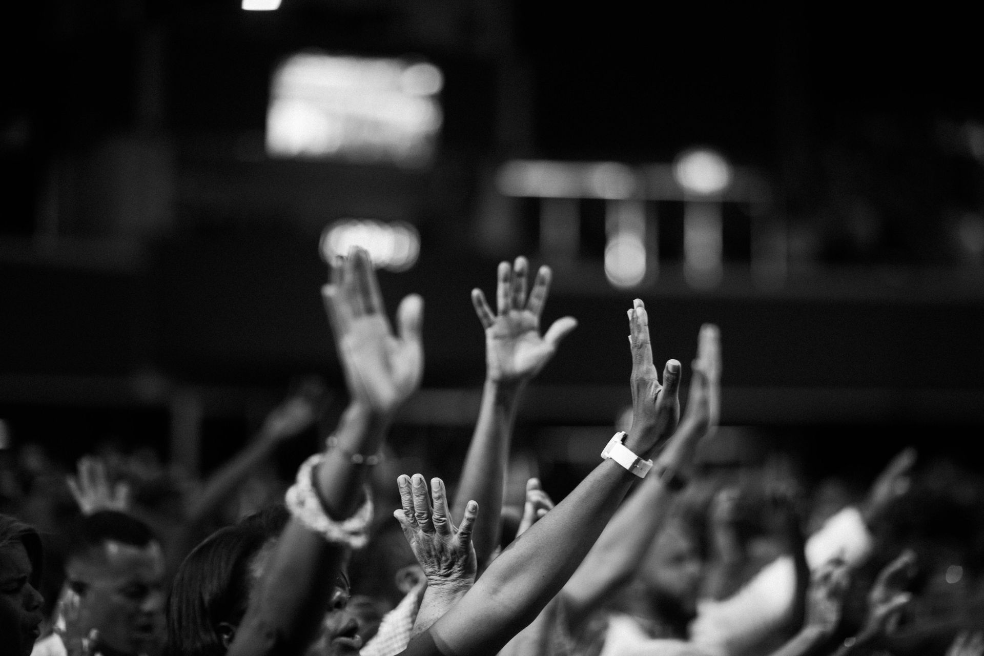 People raising their hands in a crowded room. Black and white.