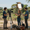 Equipo de filmación instalando una cámara y la iluminación en un lugar arenoso al aire libre con bolsas de equipo cerca.