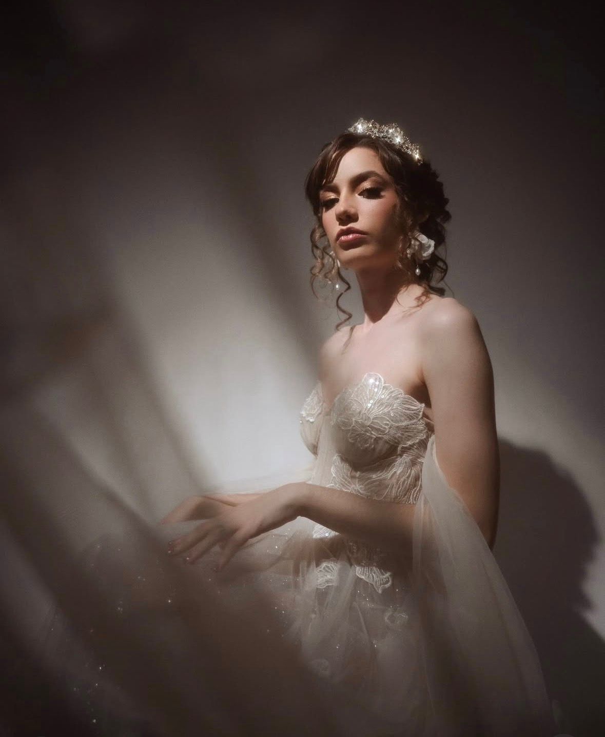 Mujer con un vestido blanco sin tirantes posando bajo una suave luz de estudio, con una tela transparente a su alrededor.