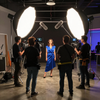 Un equipo de filmación graba a una mujer con un vestido azul en un estudio con luces brillantes y cámaras.