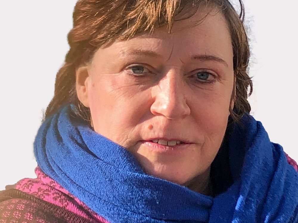 Eine Frau mit einem blauen Schal um den Hals lächelt in die Kamera.