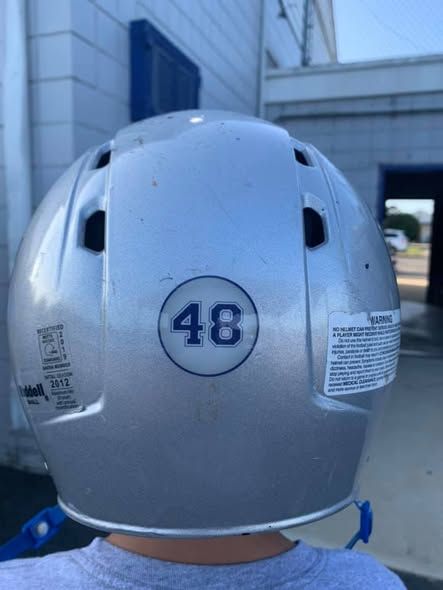 Silver football helmet with the number 48 on the back, blue chinstrap, against a white and blue building.