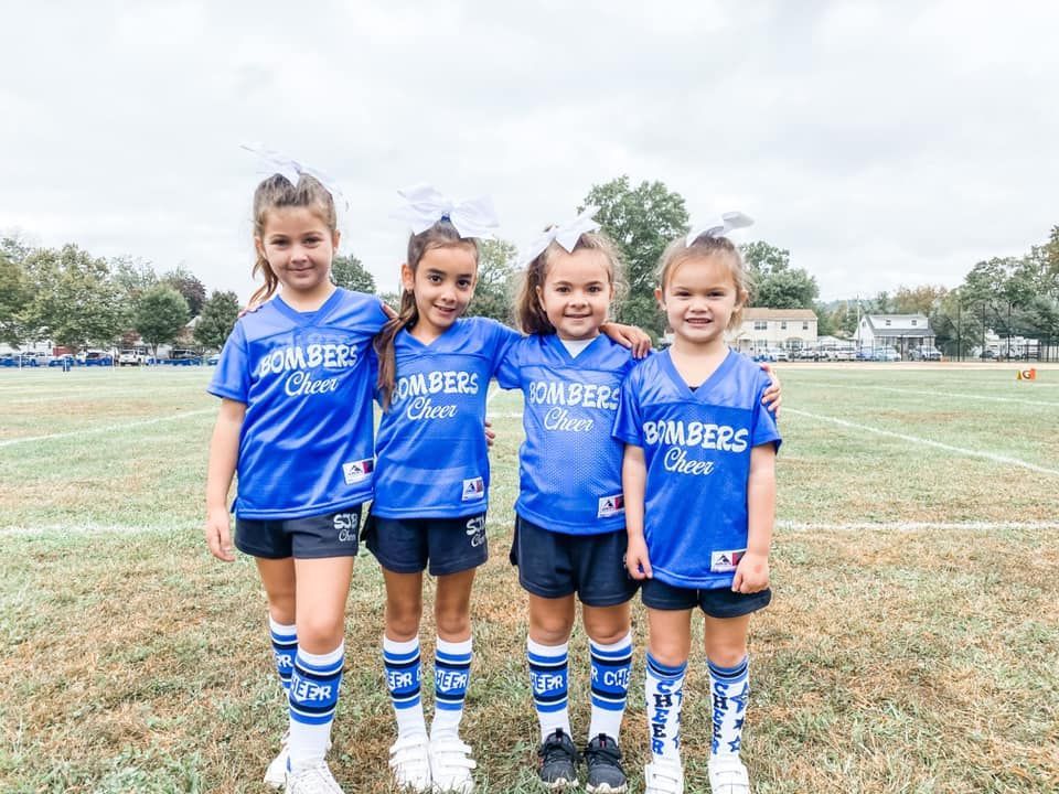 Four young cheerleaders in blue uniforms pose on a grassy field.