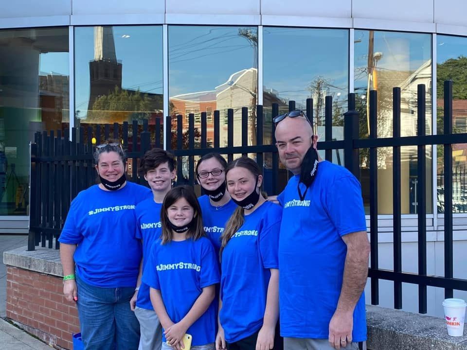 Six people in blue t-shirts stand in front of a building with a black fence.
