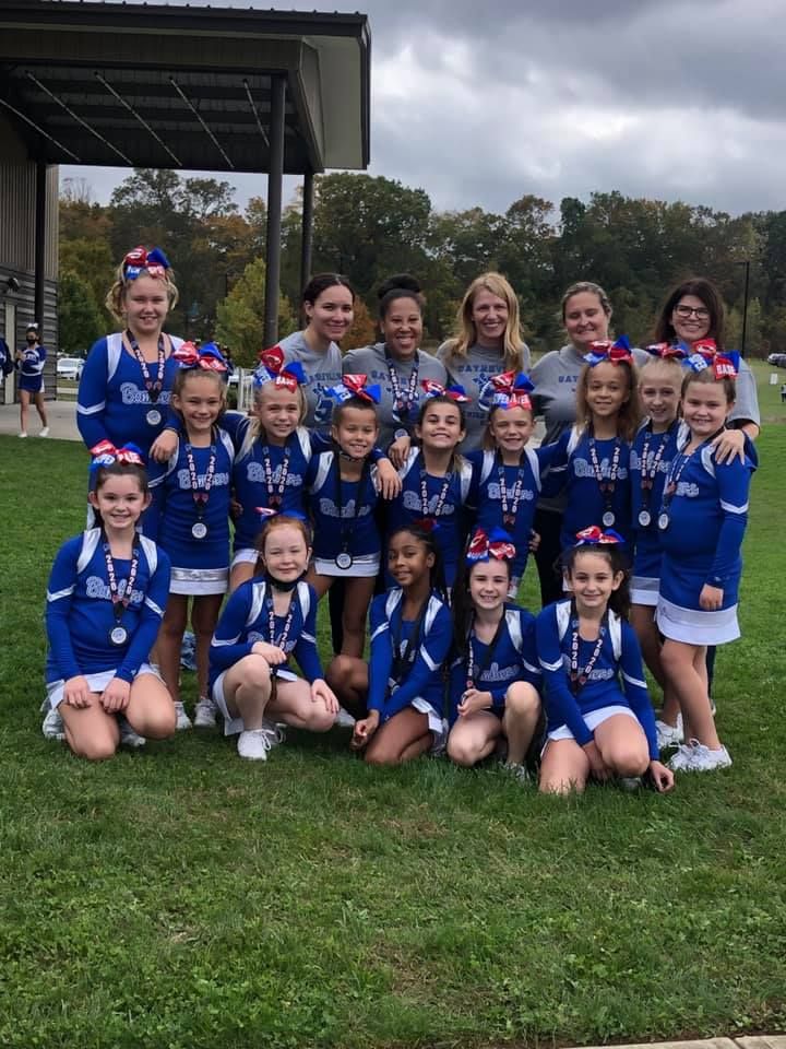 Cheerleading team posing outdoors in blue uniforms with medals.