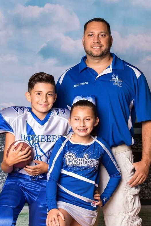 Coach with two children, one in football uniform, the other in cheerleading uniform; blue and white.