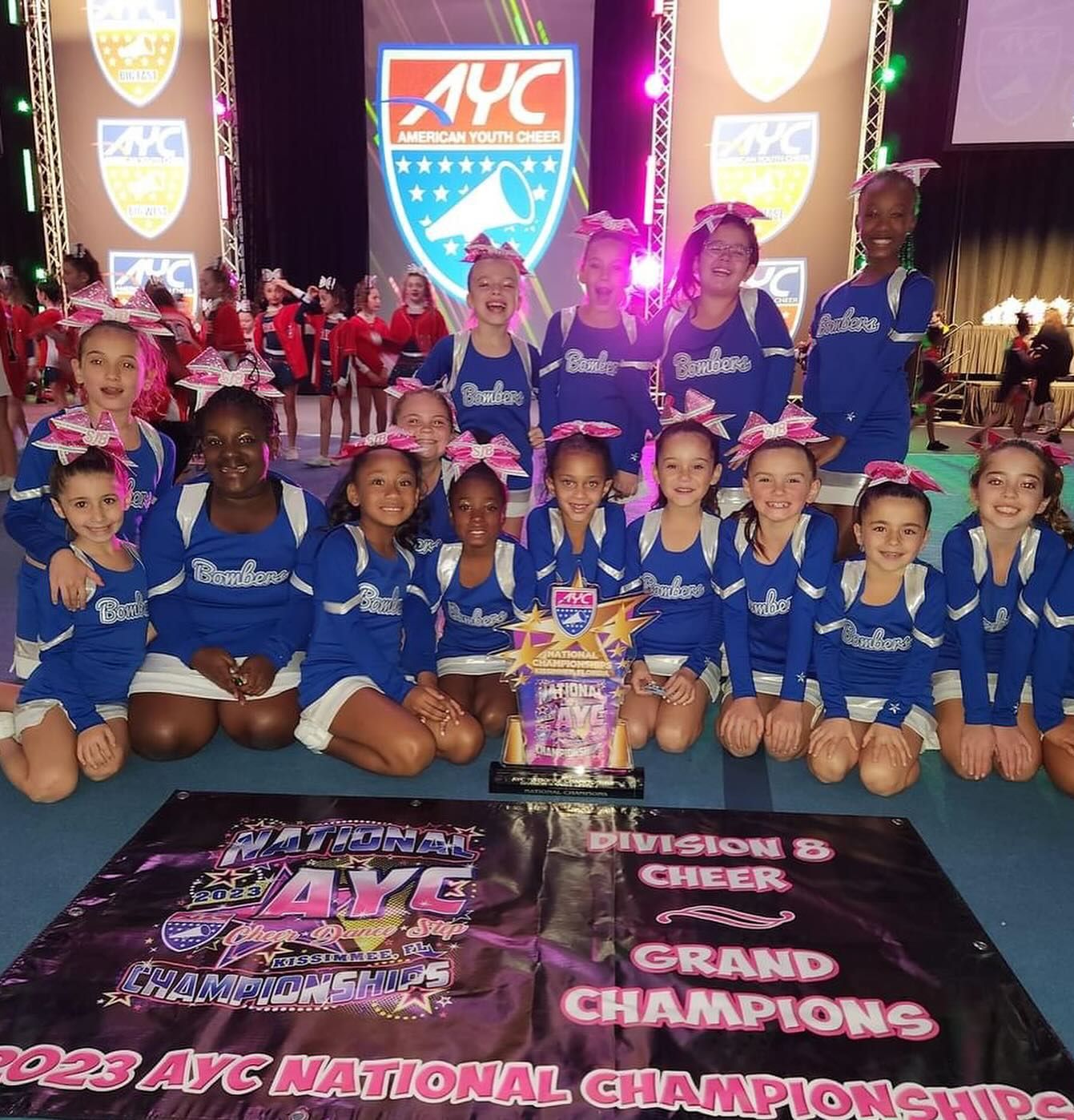 Cheerleaders in blue posing with trophy; AYC Nationals banner in foreground.