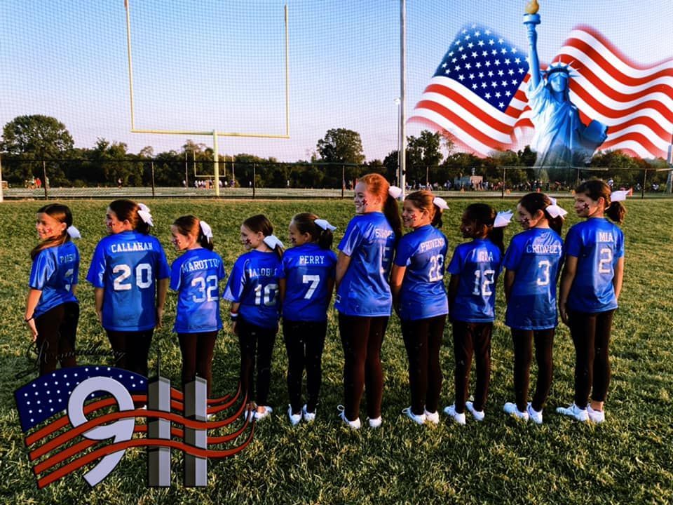 Youth cheerleaders in blue jerseys stand on a field with an American flag and Statue of Liberty superimposed. 