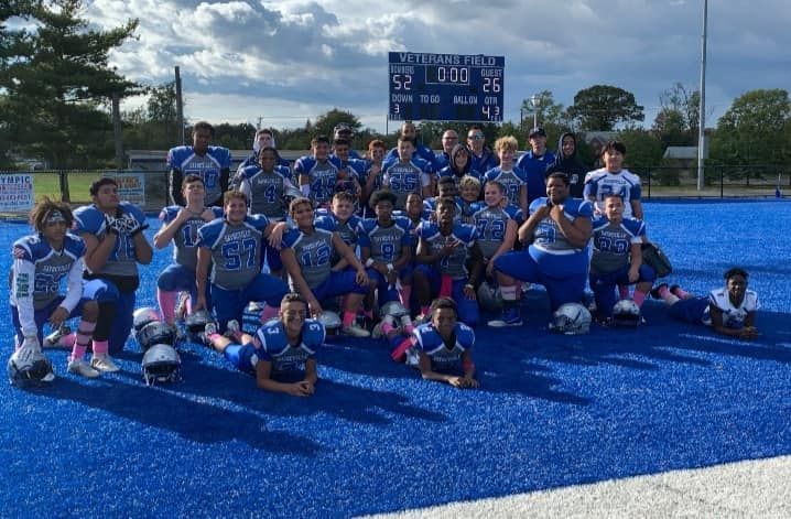 Football team in blue uniforms on blue field, posing near scoreboard.