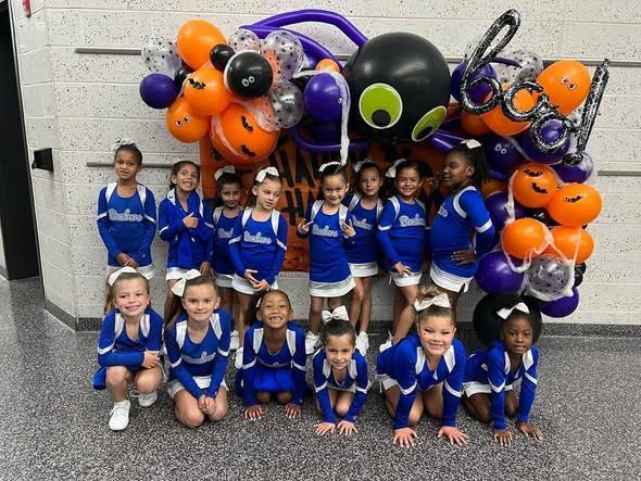 Cheerleaders in blue and white uniforms pose with Halloween balloon decorations.