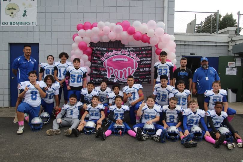 Youth football team in blue and pink uniforms posing in front of a pink balloon arch.