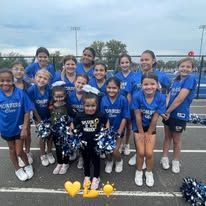 Cheerleaders in uniforms pose with pom-poms on a field.