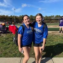 Two girls in blue shirts smiling outdoors with a sports field in background.