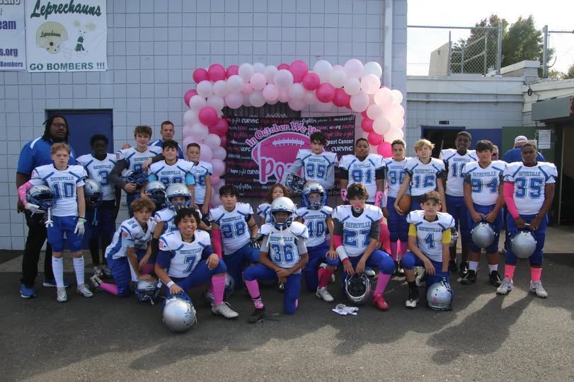 Youth football team poses with pink accents, balloons, and banner.