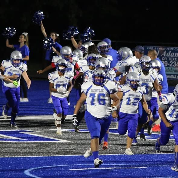 Football team in blue uniforms runs onto a blue field, cheerleaders wave pompoms.