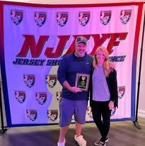 Man and woman holding an award in front of a NJYF banner.