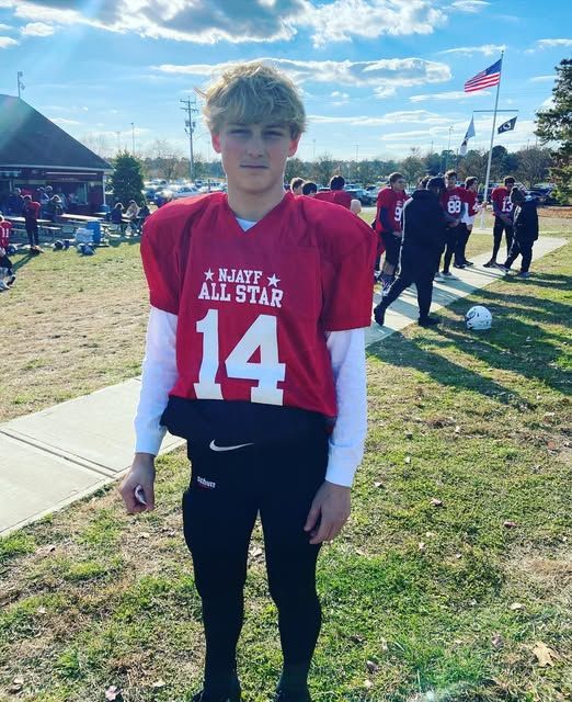 Football player in a red jersey with the number 14, standing outside on a sunny day.