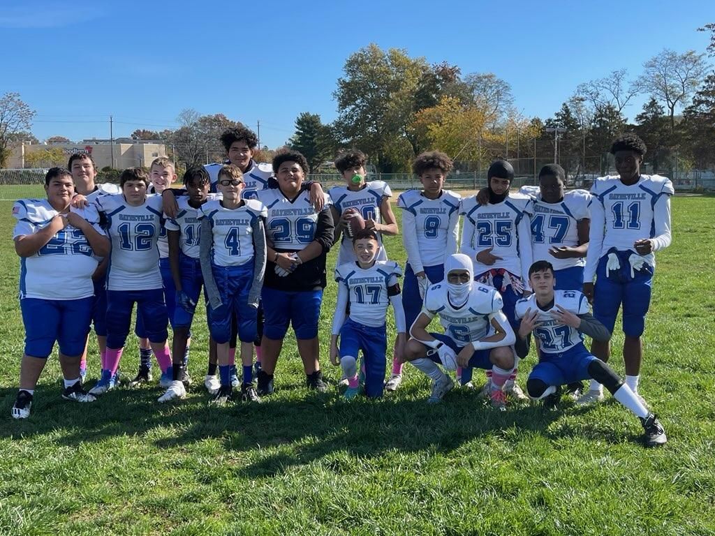 Youth football team in blue and white uniforms on a sunny field, posing for a group photo.
